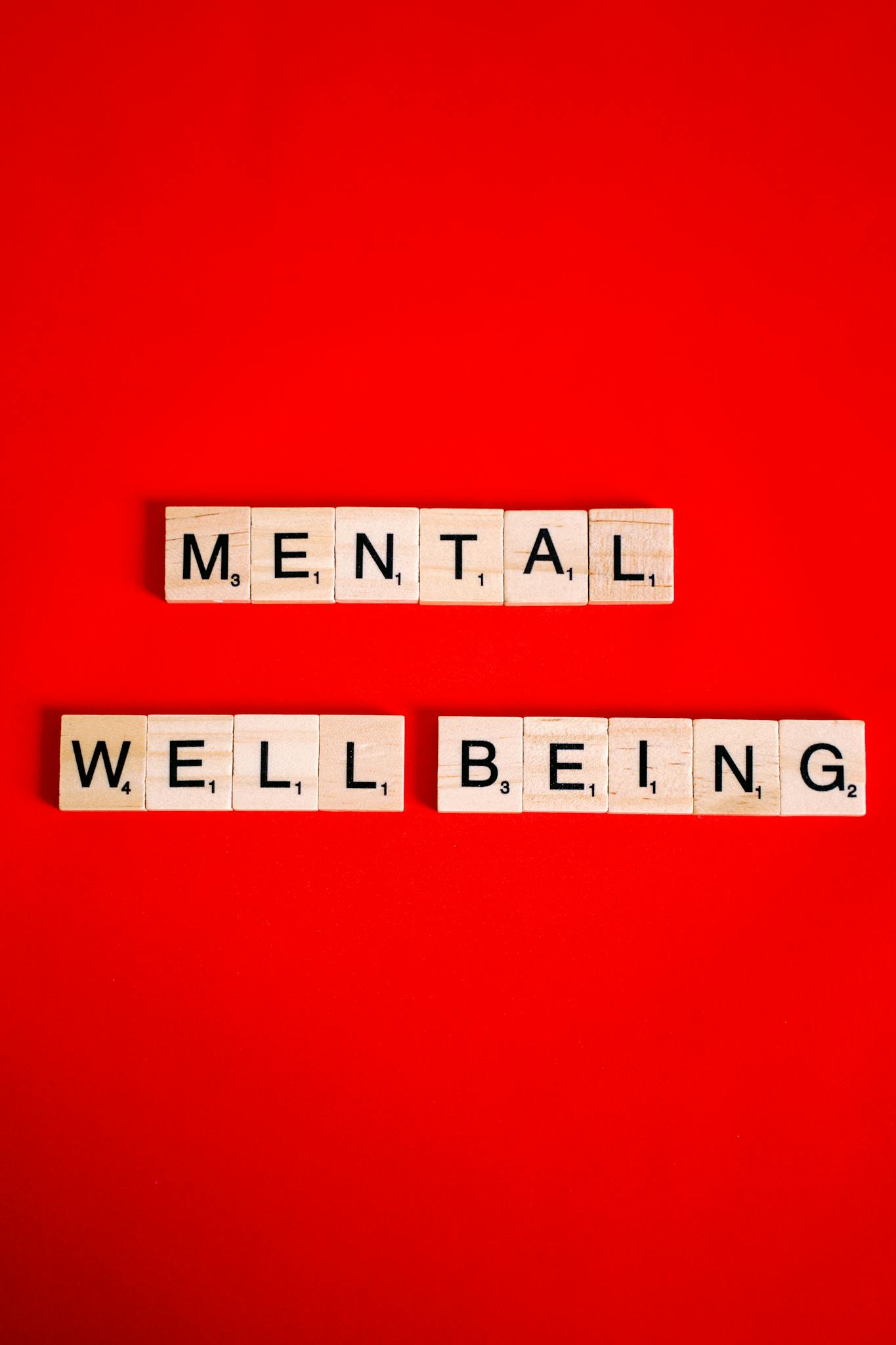 Scrabble tiles spelling 'mental well-being' on a red background, symbolizing mental health.